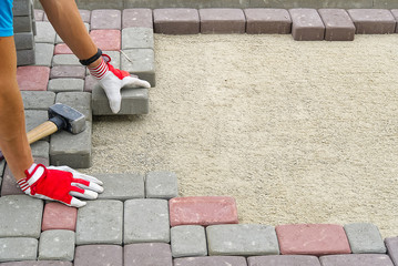 worker laying paving stones. stone pavement, construction worker laying cobblestone rocks on sand.