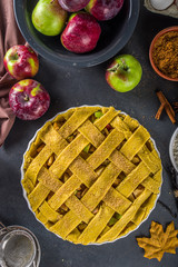 Autumn apple pAutumn apple pie cooking background. Baking background with raw traditional classic apple pie, baking ingredients and utensils, black concrete background copy spaceie cooking background