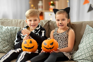 halloween, holiday and childhood concept - smiling little boy and girl in costumes with jack-o-lantern pumpkins having fun at home