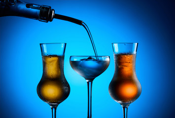 Strong alcoholic drink is poured from the bottle into glasses with ice.