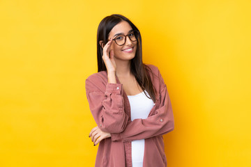 Young brunette woman over isolated yellow background with glasses and happy