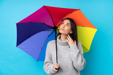 Young brunette woman holding an umbrella over isolated blue wall thinking an idea © luismolinero
