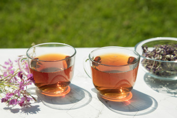 Chamaenerion angustifolium tea (Cypress, pink willow, Ivan-tea) with dry and fresh flowers for decoration in two glass cups on a light background . Concept of herbal medicine. 