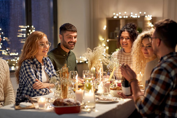 holidays and celebration concept - happy friends having christmas dinner at home with bottle of non-alcoholic red wine