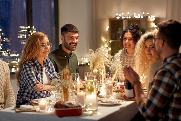 holidays and celebration concept - happy friends having christmas dinner at home with bottle of...