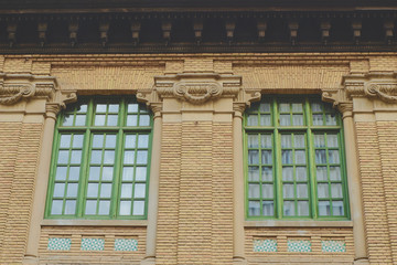 Two closed windows in green wooden frames on light brick wall.