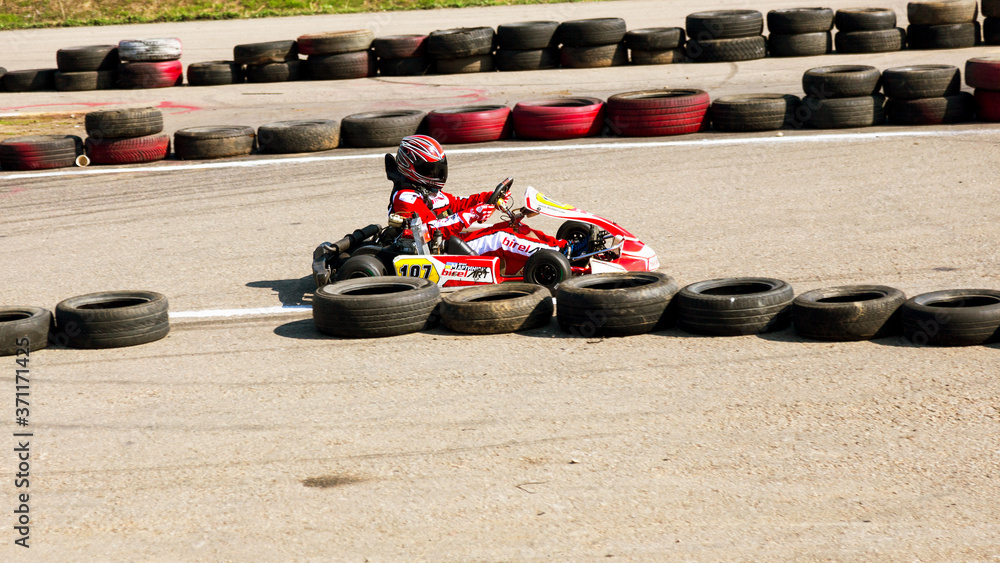 Wall mural ODESSA, UKRAINE - APRIL 2, 2017: Competitions on the picture, pilots in helmet and in racing clothes participate in the card race. Carting show. Children and adult racers on bright branded maps.