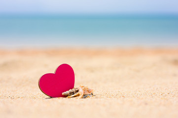 One small  seashell and pink heart lie on a sandy beach. In the background, the blue sea. Focus on seashells, blurred background.