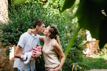 The father, mother holds little newborn girl on background wall outdoors. Portrait of dad, mom and daughter. The concept of family holiday. Closed eyes and sleep. upper half. Close up.