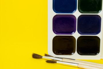 multicolored watercolor paints with brushes on yellow background