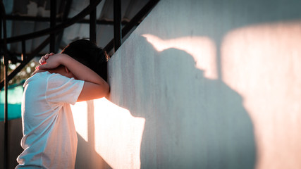 Depressed, frustrated and overwhelmed Asian teenage boy stand alone and lean his head against wall with casting shadow, feeling worthless, stressed, guilty, hopeless and having suicidal thought. - obrazy, fototapety, plakaty