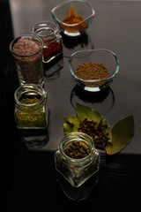 various spices in glass bowls and jars on a black background
