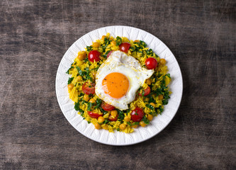 Chinese fried rice with turmeric, chickpeas, tomatoes, kale and with fried eggs on white ceramic plate on dark wooden background. Quick and easy dinner. Flat lay, space