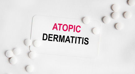 On the card is the inscription ATOPIC DERMATITIS, the first word is highlighted in red, next to lie white tablets.