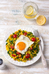 Chinese fried rice with turmeric, chickpeas, tomatoes, kale and with fried eggs on white ceramic plate on wooden background