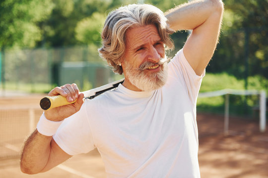 Senior modern stylish man outdoors on the tennis coart at daytime and holding racket