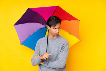 Man holding an umbrella over isolated yellow background thinking an idea
