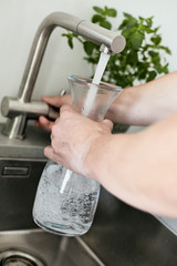 Person, die sich am Wasserhahn ein Glas mit Leitungswasser befüllt