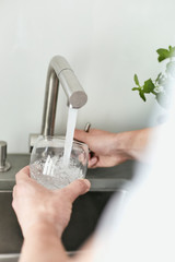 Person, die sich am Wasserhahn ein Glas mit Leitungswasser befüllt