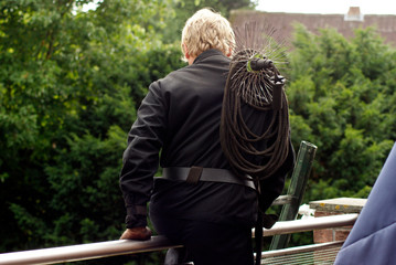 Ein blonder Schornsteinfeger steigt mit seiner Ausr&uuml;stung zum Kamin kehren &uuml;ber der Schulter &uuml;ber ein Gel&auml;nder.