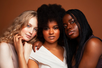 young pretty caucasian, afro, scandinavian woman posing cheerful together on brown background, lifestyle diverse nationality people concept