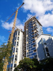 Obraz na płótnie Canvas Moderner Neubau eines Apartmenthaus mit zwei Hochhaus Türmen mit gelbem Baukran vor blauem Himmel mit weißen Wolken im Westend von Frankfurt am Main in Hessen