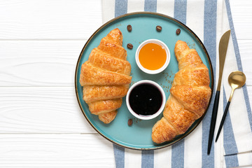 Fresh french croissants with chocolate on blue plate, blueberry jam, spoon, honey, napkin coffee grains on white background Continental morning breakfast Top view Flat lay