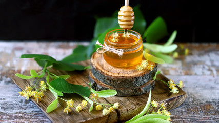 Selective focus. Honey stick, jar of linden honey, linden flowers. Linden honey.