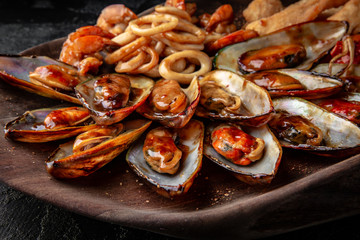 Delicious cooked mussels in sauce with dried baguette. Sea food serving in a wooden plateau
