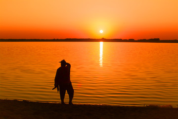 a silhouette of a man looks at the sunset by the lake