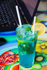 Blue cocktail with curacao and citruses and notebook background, working space. Alcoholic drink. Summer holidays.