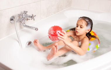 Little girl have fun in the bathtub and plays in the inflatable red ball while sitting in the...