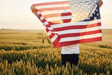 View from behind. Holding USA flag in hands. Patriotic senior stylish man with grey hair and beard on the agricultural field