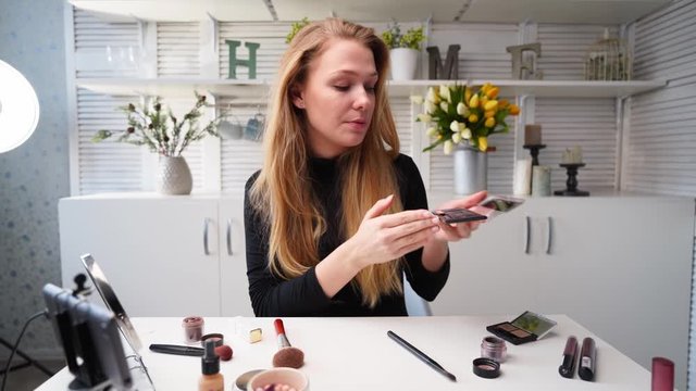 Beauty blogger woman filming daily makeup routine tutorial near camera. Influencer girl live streaming cosmetics product review. Vlogger female recommends eye shadow palette, teaches in masterclass.