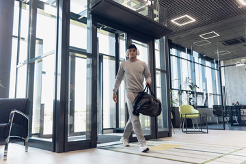 Entrance. Sportsman walking down in modern glassed building, airport in megapolis. Before flight to competition. Professional stylish, confident athlete. Journey, vacation, sport lifestyle.