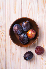Obraz premium Fresh sweet plum fruits in brown wooden bowl, wood table background, top view
