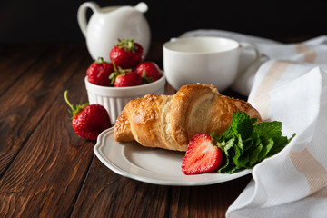 Fresh golden croissants with strawberries on dark slate board. Breakfast time. Top view