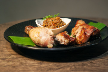 Thai grilled chicken wing on bamboo leave with traditional Thai blend of Fermented fish spicy dip on black plate isolated on Dark Slate Gray Concrete Wall background