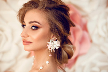 Beautiful young bride with makeup and fashion wedding hairstyle. Closeup portrait of young gorgeous woman over roses flowers. Studio shot.
