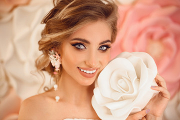 Obraz na płótnie Canvas Beautiful young bride with makeup and fashion wedding hairstyle. Closeup portrait of young gorgeous woman over roses flowers. Studio shot.