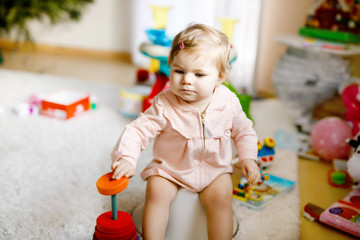 Fototapeta premium Closeup of cute little 12 months old toddler baby girl child sitting on potty. Kid playing with educational wooden toy. Toilet training concept. Baby learning, development steps