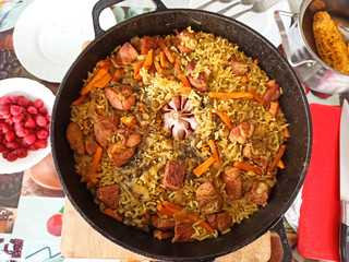 Close-up delicious pilaf in a cauldron. Appetizing Uzbek pilaf from rice and pork. Head of garlic...
