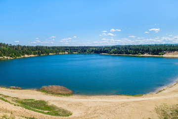 Dark blue lake surrounded by pine forest. Lake arose on site of former industrial quarry