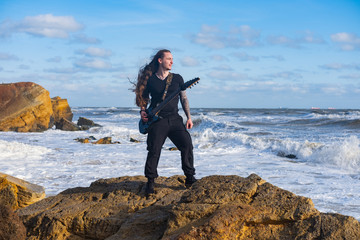 Young male in black and long hair play on guitar on the beach