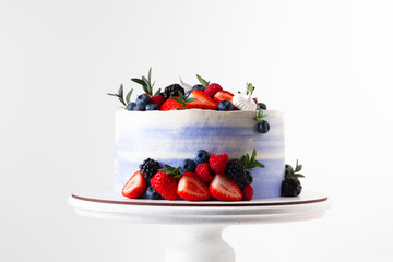 Blue cake with strawberries, raspberries and blueberries decoration on the white stand isolated on the white background