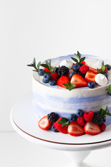 Blue cake with strawberries, raspberries and blueberries decoration on the white stand isolated on the white background