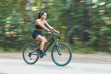 Fototapeta premium girl quickly rides a bicycle in the forest