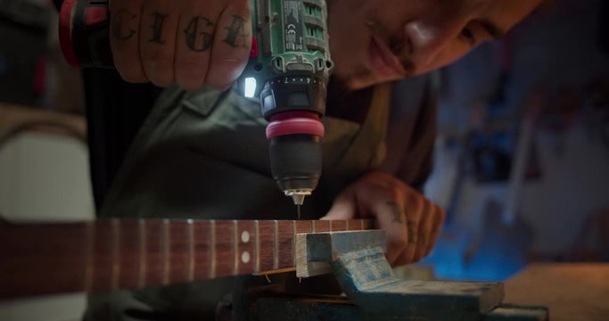 Close up of handsome powerful joiner male artisan drilling thin screw in wooden guitar, work process of confident young Hispanic guy making musical instrument using drill tool for wooden planks