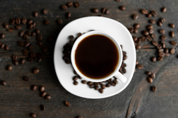 Coffee cup with roasted coffee beans on wooden table background. Mug of black coffe with scattered...