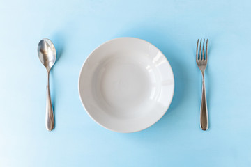 empty plate, spoon and fork on light blue background